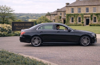 Black private hire saloon outside a country house