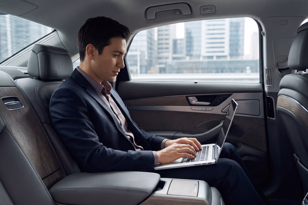 Business passenger working on a laptop in the rear of an executive chauffeur car on the way to Stansted Airport